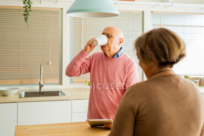 Couple d'âge mûr utilisant smartphone et tablette tout en passant du temps le matin dans la cuisine ensemble — Photo de stock