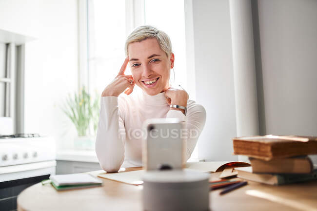Female blogger talking about astrology while recording video on cellphone at desk in sunlight — Stock Photo