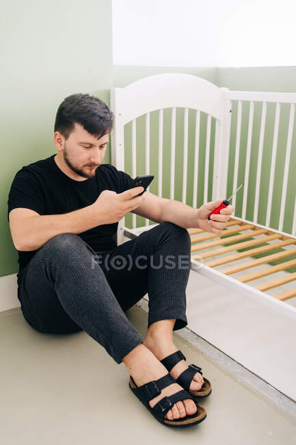 Чоловік спілкується на мобільному телефоні проти ліжечка в кімнаті — стокове фото