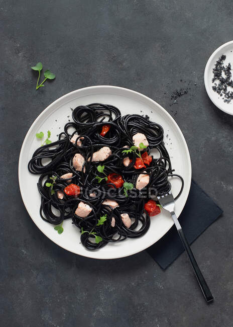 Зверху чорне чорнило спагетті з лососем у керамічній тарілці на темному фоні — стокове фото