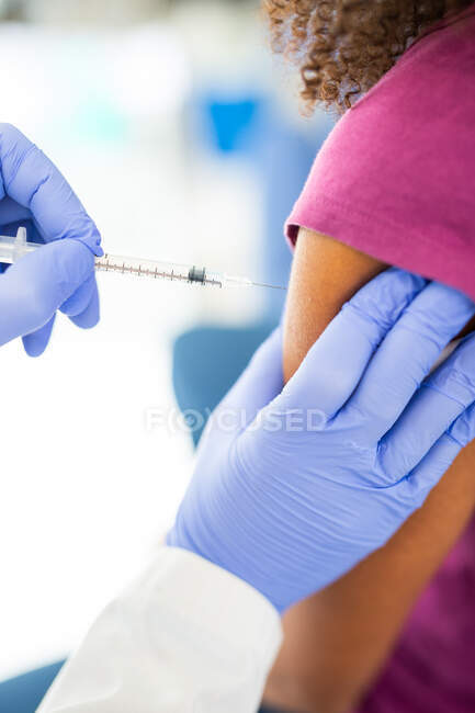 Нерозбірлива жінка-медик у захисній формі та латексних рукавичках вакцинує анонімного афроамериканського пацієнта у клініці під час спалаху коронавірусу. — стокове фото