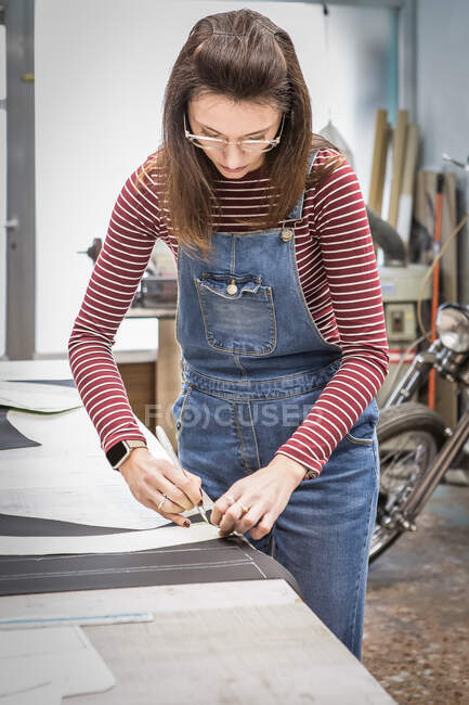 Concentrated female sewer making marks on piece of leather while creating upholstery for motorcycle seats in workshop — Stock Photo