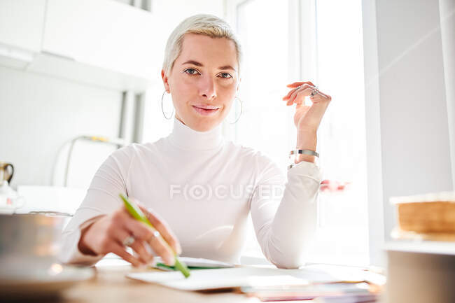 Счастливая женщина-астролог с короткими волосами в кольцах смотрит в камеру за столом в солнечный день — стоковое фото