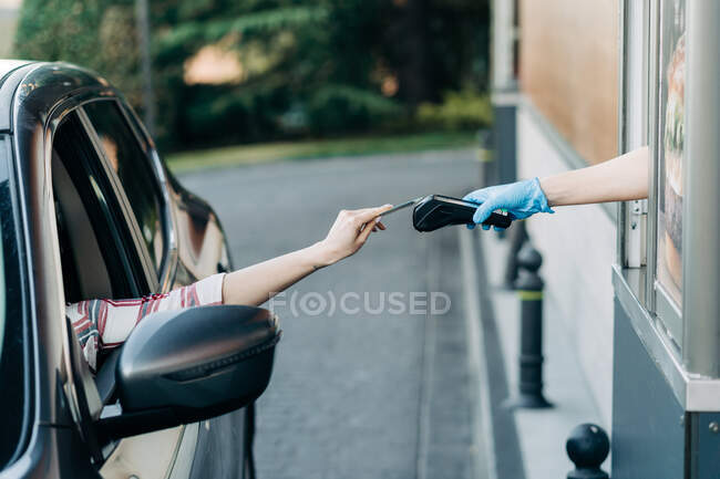 Crop unrecognizable person paying with plastic card on POS terminal in drive through fast food cafe — Stock Photo