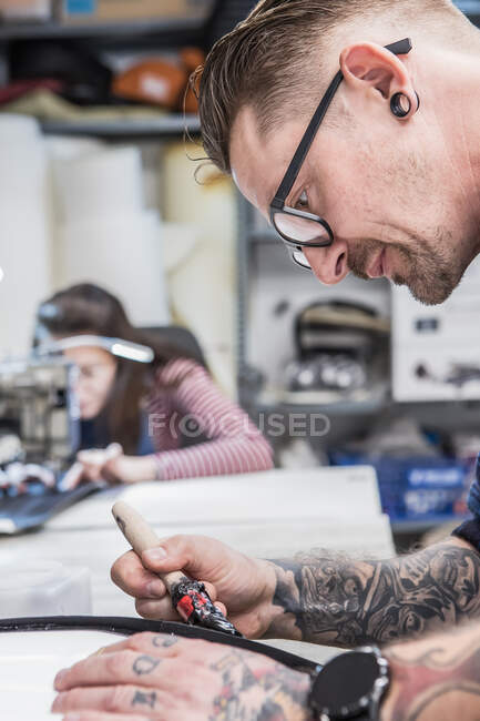 Seitenansicht tätowierter Handwerker, der beim Polstern an der Werkbank Kleber auf Motorradsitz aufträgt — Stockfoto
