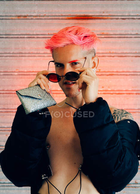 Jovem gay no elegante desgaste com tatuagem e rosa cabelo segurando bolsa enquanto olhando para câmera — Fotografia de Stock