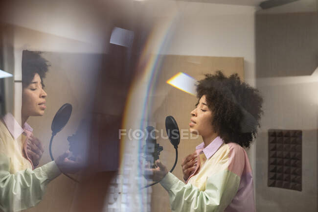Vue de côté de la jeune chanteuse afro-américaine chantant en micro avec filtre pop en studio d'enregistrement — Photo de stock