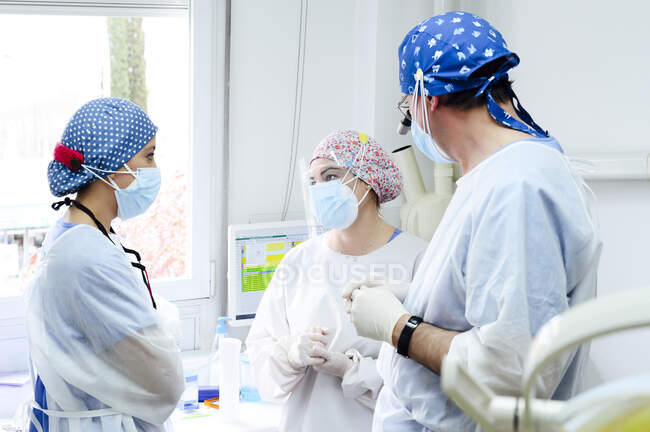 Анонимный хирург-мужчина в медицинском бинокле разговаривает с коллегами в стерильных масках, глядя друг на друга в больнице — стоковое фото