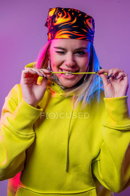 Жінка в одязі вуличного стилю дивиться на камеру на фіолетовому фоні в студії з неоновим освітленням — стокове фото