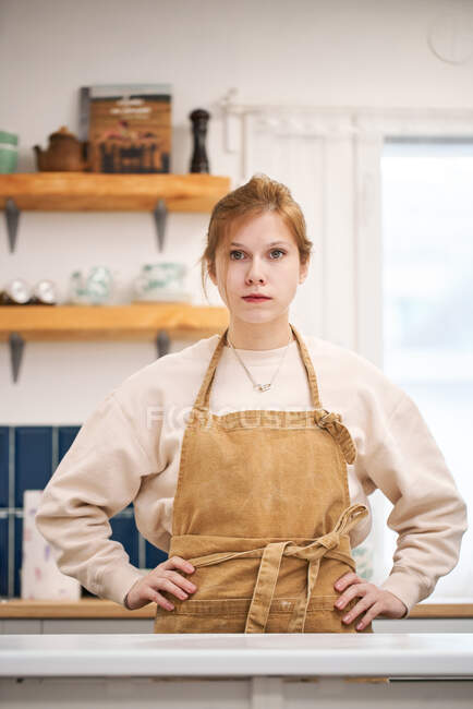 Молодая самоуверенная женщина с руками на бедрах смотрит в камеру за столом в светлом доме — стоковое фото