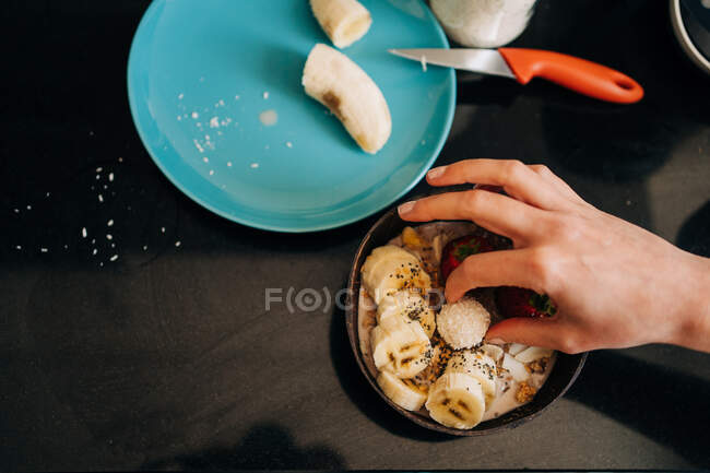 Top view crop unrecognizable person topping tasty healthy porridge with banana and strawberries in kitchen — Stock Photo