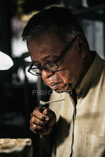 Concentrated senior African American male goldsmith in casual clothes and eyeglasses holding solder with pliers while creating jewelry in workshop — Stock Photo
