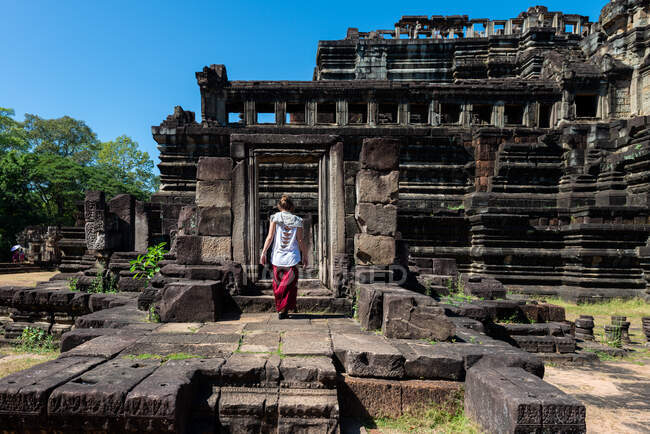 Visão traseira do turista feminino anônimo em pé contra a fachada do templo de pedra envelhecida em Angkor Wat do Camboja — Fotografia de Stock