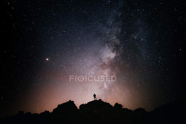 Silhouette de touriste anonyme debout sur une falaise contre un ciel étoilé brillant la nuit — Photo de stock