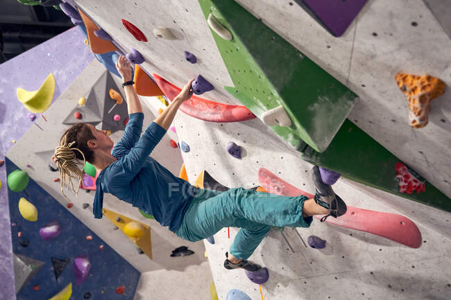 Enduring female alpinist in activewear climbing artificial boulders while training in bouldering gym — Stock Photo