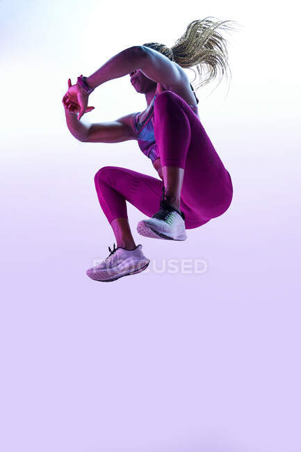 Анонимная афроамериканка-спортсменка с летящими волосами в спортивной одежде, прыгающая с сжатыми руками во время тренировки — стоковое фото