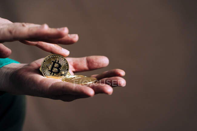 Crop unrecognizable dealer with metal crypto coins with letter and ornament on golden surface — Stock Photo