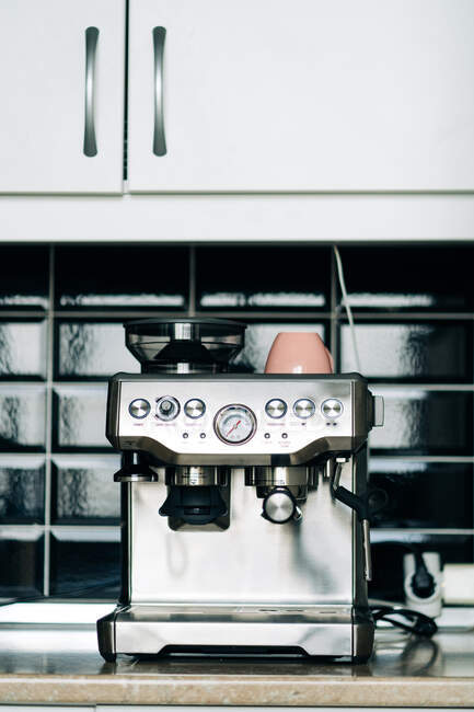 Machine à café professionnelle en acier inoxydable avec manomètre et tasse en céramique sur la table contre le mur de briques de verre dans la maison — Photo de stock