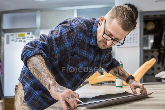 Alcantarillado masculino de vista lateral que hace pieza de tela mientras trabaja en el taller y crea tapicería para asientos de motocicleta - foto de stock