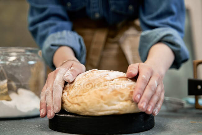 Crop femme anonyme avec pain de blé frais entier avec croûte à table pendant le processus de cuisson — Photo de stock