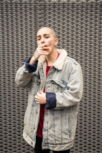 Selbstbewusste junge Transgender in Jeansjacke rauchen Zigarette, während sie in die Kamera schauen — Stockfoto