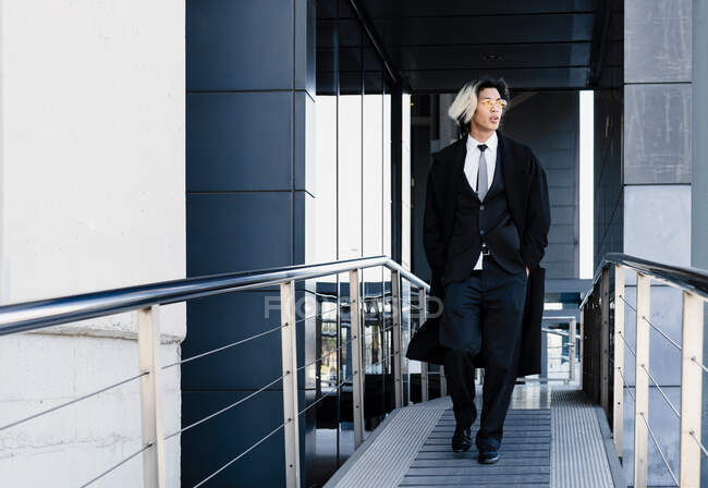 Young Asian male executive in suit and sunglasses with hands in pockets looking away between handrails in town — Stock Photo