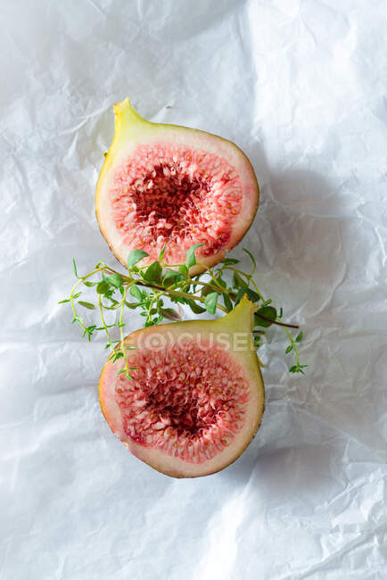 Overhead view of tasty ripe fig slices with aromatic thyme sprigs on baking paper — Stock Photo