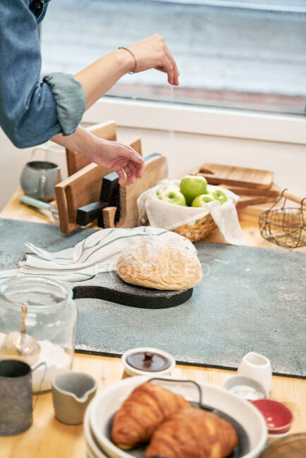 Анонимные урожаи женщин посыпать свежий хлеб пшеницы с мукой во время приготовления пищи на домашней кухне — стоковое фото