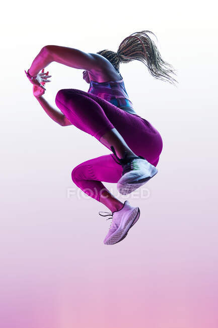 Анонимная афроамериканка-спортсменка с летящими волосами в спортивной одежде, прыгающая с сжатыми руками во время тренировки — стоковое фото