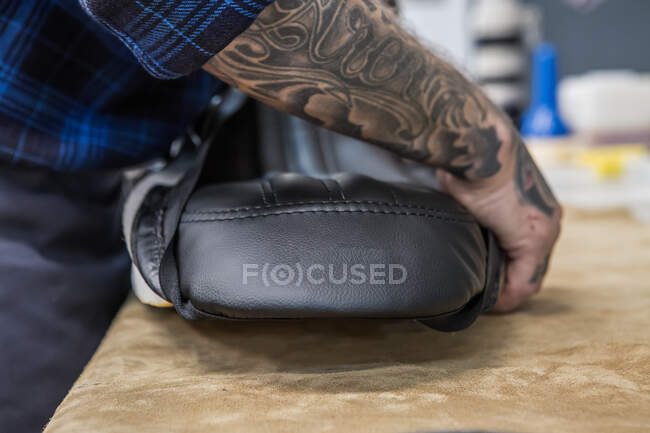 Side view of crop unrecognizable male artisan putting on handmade leather upholstery on motorbike seat while standing at workbench in workshop — Stock Photo