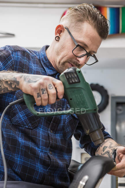 Focused male artisan using heat gun while making leather upholstery for motorbike seat in workshop — Stock Photo