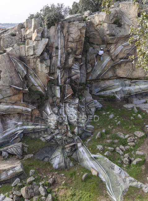 Drone view of man in helmet hanging on rope while painting graffiti on steep stony slope — Stock Photo