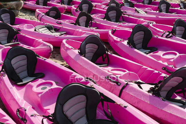 Many empty kayak boats of bright pink color placed on sandy seashore on sunny weather in Malaga Spain — Stock Photo
