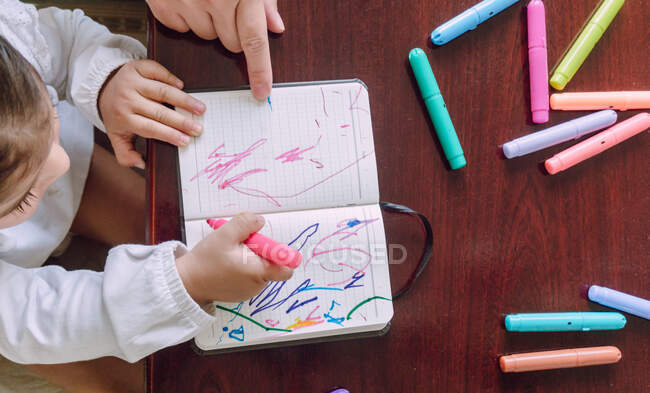 Ritaglia donna irriconoscibile e bambino seduto a tavola e disegno con pennarelli nel quaderno — Foto stock