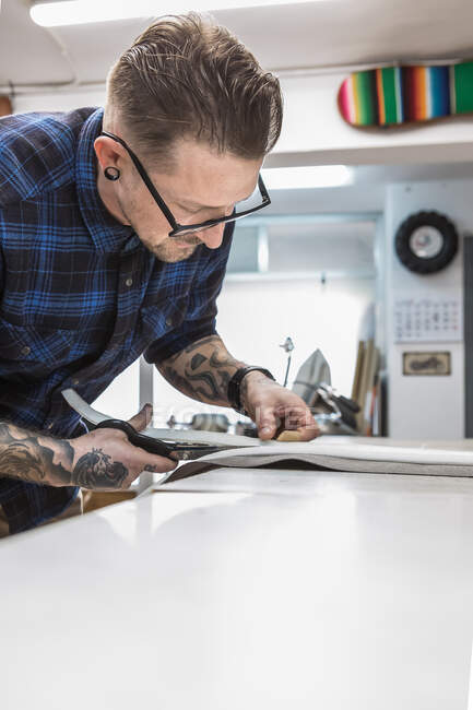 Peça de corte de artesanato masculino empanado na bancada de trabalho enquanto prepara materiais para criar estofos de assento de motocicleta na oficina — Fotografia de Stock