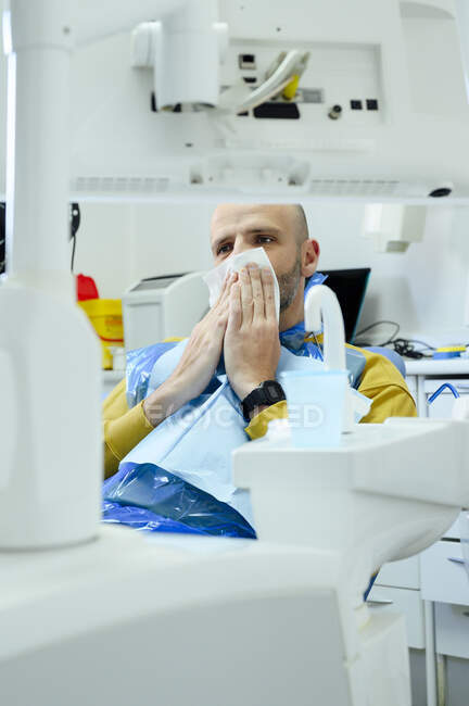 Cultivo hombre maduro que cubre la cara con servilleta mientras mira hacia adelante después del tratamiento dental en el hospital - foto de stock