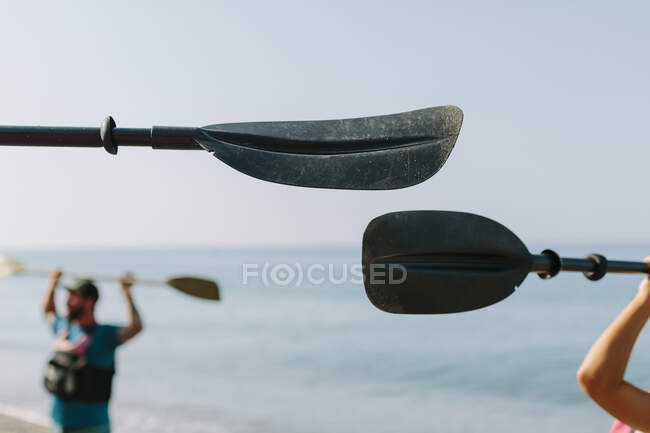 Anonymous people raising arms with kayak paddles and standing on blue seashore on sunny day in Malaga Spain — Stock Photo