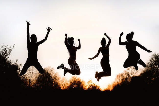 Du dessous des silhouettes des femelles sautant au-dessus du sol contre le ciel au coucher du soleil dans le parc — Photo de stock