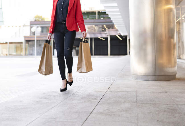 Cultivez acheteur féminin avec des sacs à provisions en papier et café à emporter debout près de vitrine du magasin en ville — Photo de stock