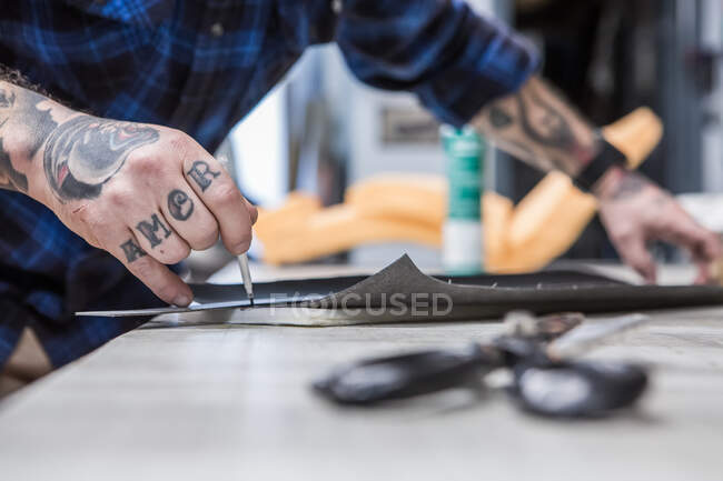 Cortar esgoto masculino irreconhecível fazendo pedaço de pano enquanto trabalhava na oficina e criando estofos para assentos de motocicleta — Fotografia de Stock