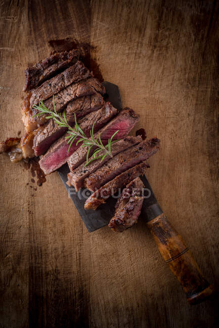 Overhead view of tasty tender meat pieces with fresh herb sprig on top on brown background with cleaver — Stock Photo