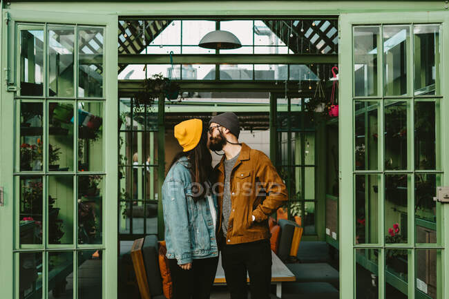 Cheerful couple of trendy hipsters standing on wooden terrace while holding hands and looking over shoulder — Stock Photo