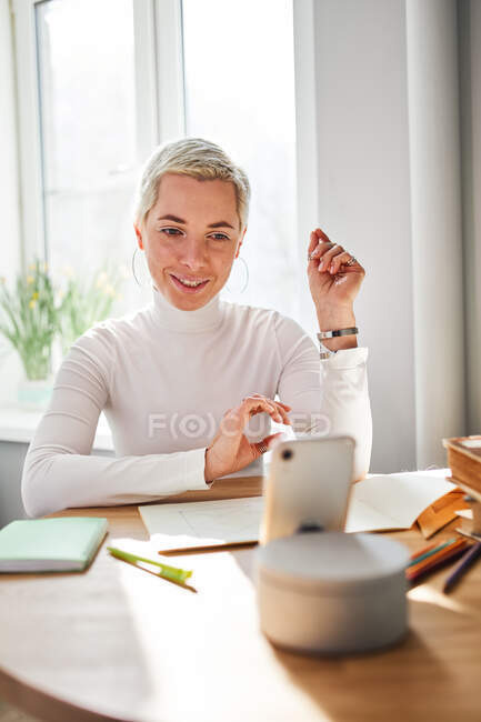 Smiling female blogger talking about astrology while recording video on cellphone at desk in sunlight — Stock Photo