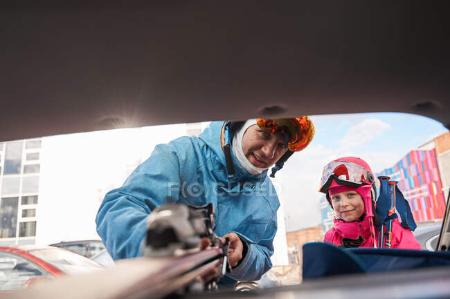 Content father and daughter wearing warm sportswear and goggles placing skis in car trunk on sunny winter day — Stock Photo