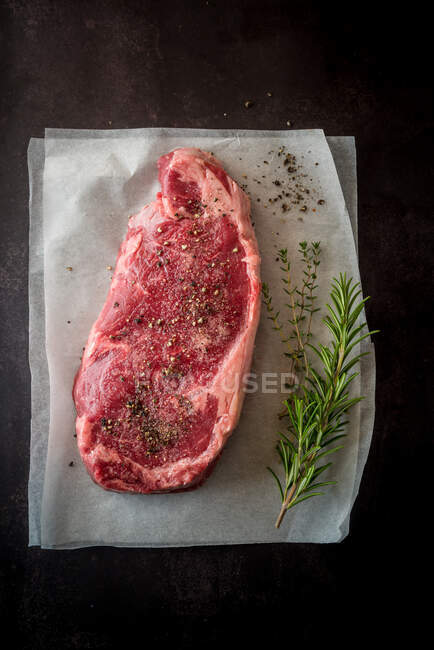 Overhead view of uncooked meat piece with thyme leaves against paper on black background — Stock Photo
