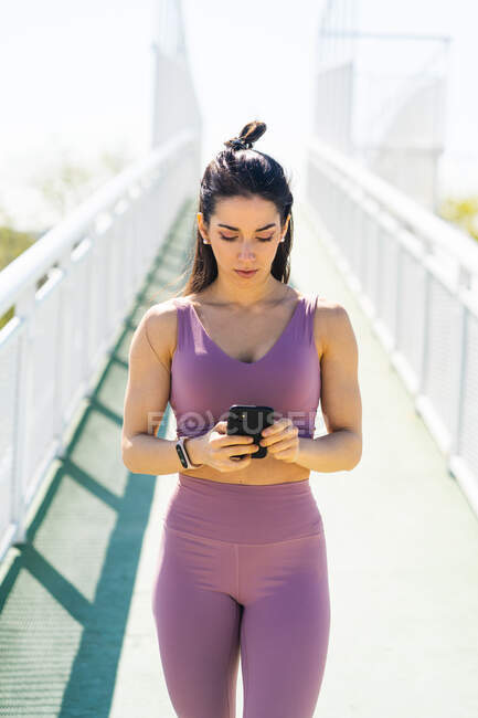 Young fit female athlete in sports clothes text messaging on mobile phone after training on sunny day — Foto stock