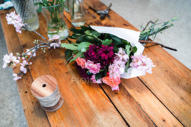 Buquê envolto elegante de alto ângulo com rosas frescas e flores rosa sortidas atadas em mesa de madeira perto de vasos de vidro na loja — Fotografia de Stock
