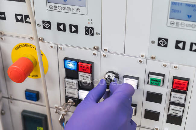 Crop unrecognizable professional male laboratory assistant in white robe and latex gloves pressing buttons on modern equipment — Stock Photo