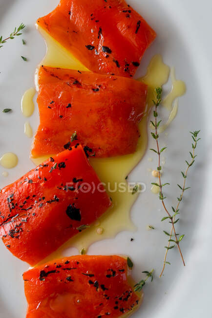 Вид сверху на вкусные кусочки красного перца со свежими веточками тимьяна и оливковым маслом на тарелке — стоковое фото