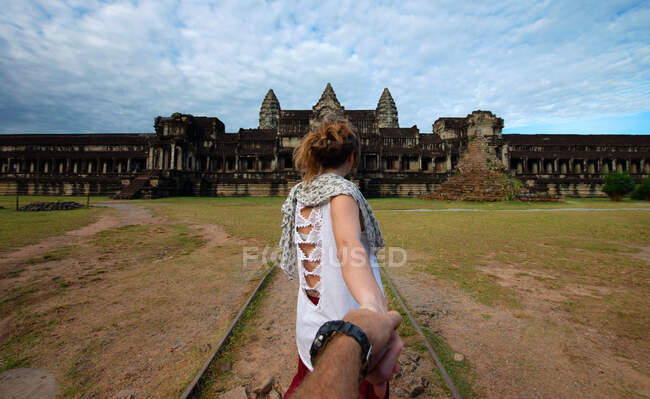 Crop turisti anonimi che si tengono per mano contro invecchiato facciata di culto in muratura sotto cielo nuvoloso in Angkor Wat della Cambogia — Foto stock